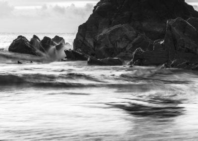 Black & White long exposure photo of waves crashing against the rocks.